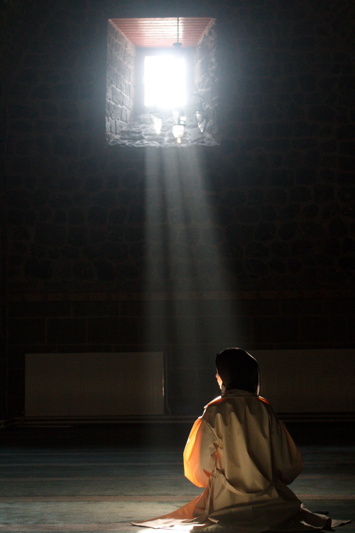 Persona orando en penumbra bajo un haz de luz