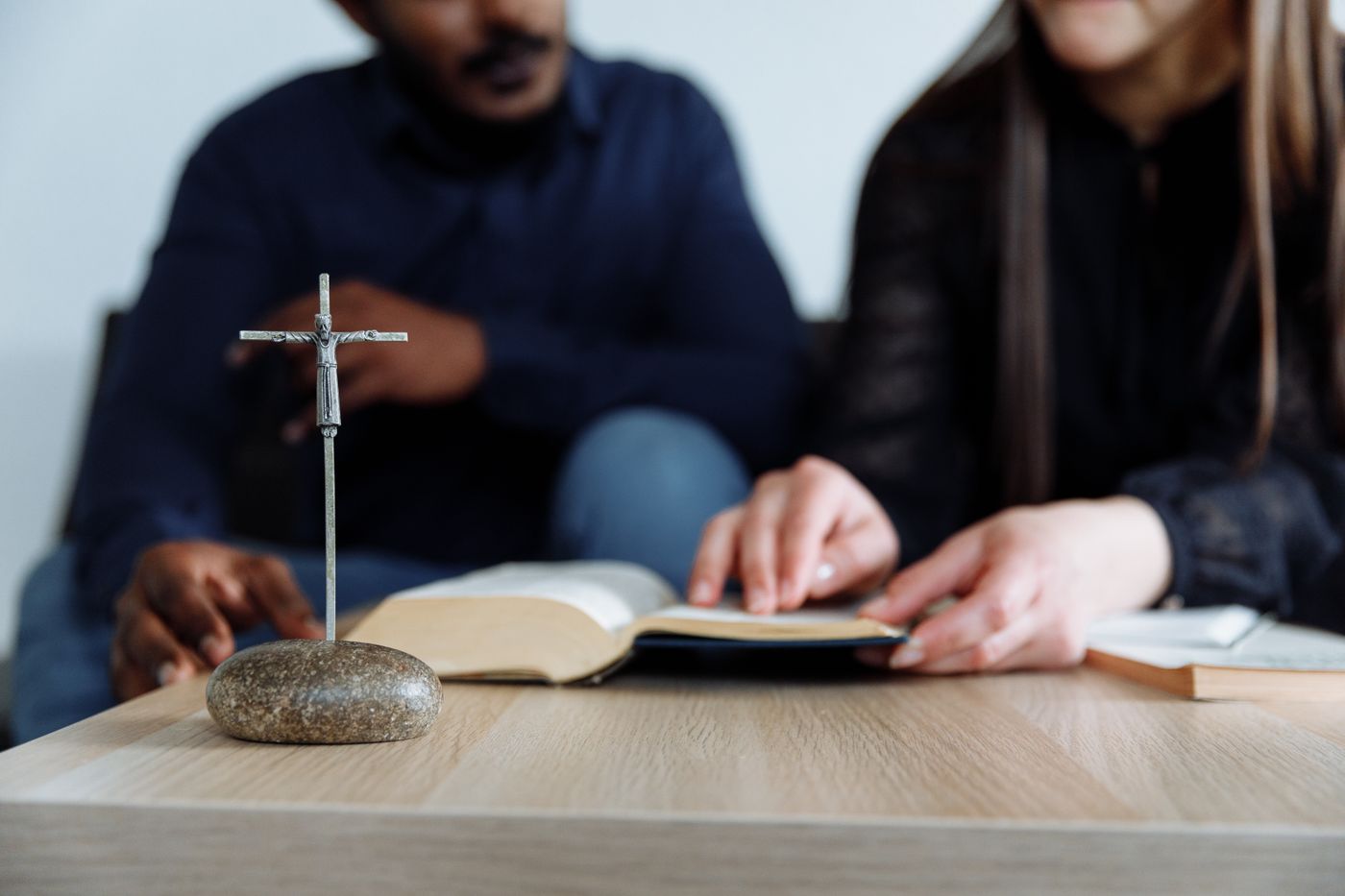 Dos personas leyendo juntas una Biblia abierta, con una cruz sobre la mesa