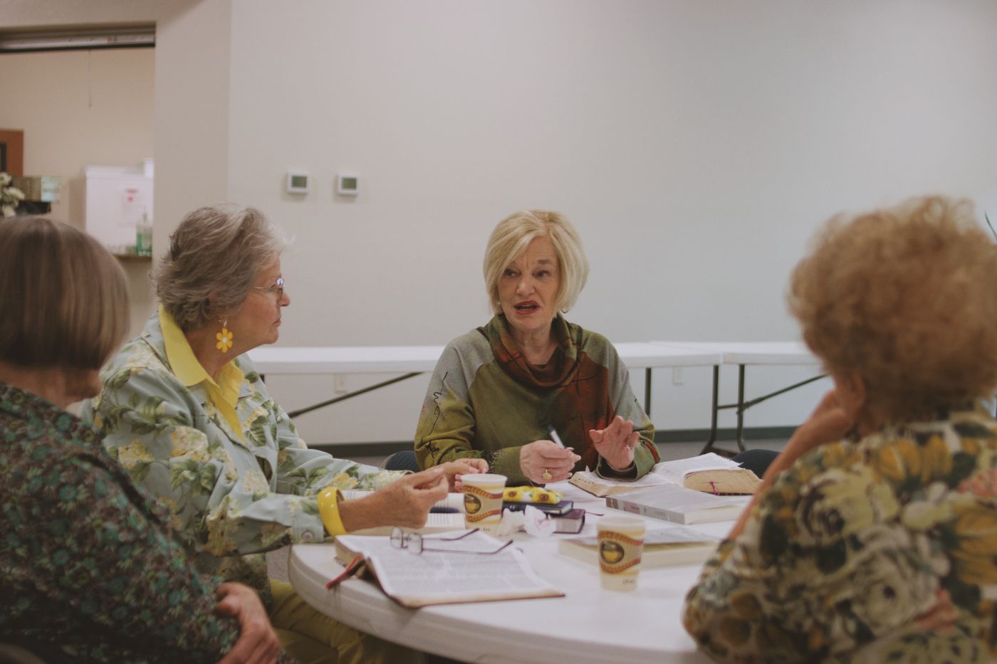 Grupo de mujeres alrededor de una mesa, conversando con sus cuadernos y Biblias